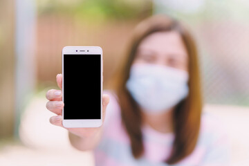 A woman holding a black blank screen in front of her to enter text on blurled background.