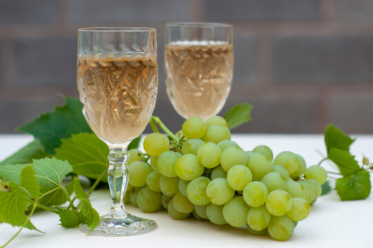 Two glasses of white wine, bunches of grapes and a young vine on a light wooden background. A horizontal snapshot.