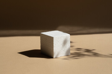 Geometric 3d foam podium for product demonstrations. White cube, in rays of sunlight, casts hard...