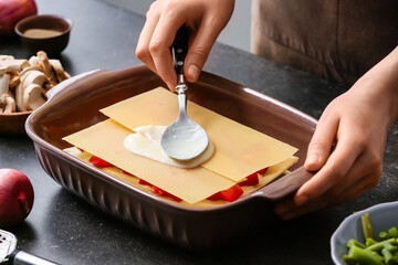 Woman preparing tasty vegetable lasagna on table in kitchen