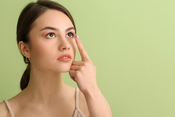 Young woman putting in contact lenses on color background