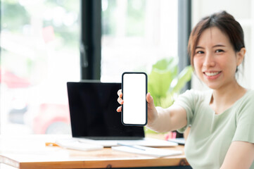 Fototapeta premium Young asian woman showing blank screen smartphone while sitting at the table in living room.