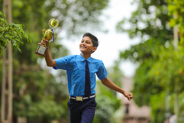 Clever schoolboy raising his trophy as a winner in school competition.