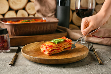 Woman putting piece of tasty tomato lasagna on plate