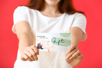 Young woman with gift voucher for massage on color background