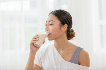 Healthy Young Asian woman Drinking milk with calcium for strong bone at home,Smiling indian woman holding soy milk on glass enjoy with nutrition wellness life,Wellness with natural milk fresh Concept