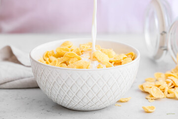 Pouring of milk into bowl with corn flakes on table, closeup