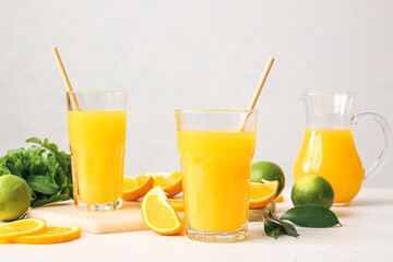 Glasses of tasty orange juice on light background