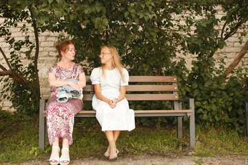 Mother and daughter talking, looking at each other on a bench in a rural place. Family members are also friends