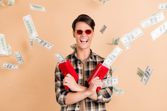 Photo of positive rich guy hold gun throw cash usd wear sunglass plaid shirt isolated beige color background