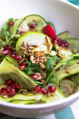 A large dish with a grilled zucchini salad with fresh cucumbers, radish, pomegranate seeds and fresh arugula.