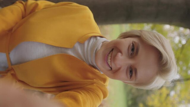 Vertical. Young caucasian woman having video call from the park. Waving to the camera