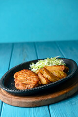 Grilled Chicken Steak with fried potatoes in rural style and coleslaw salad served in a tray over blue background.