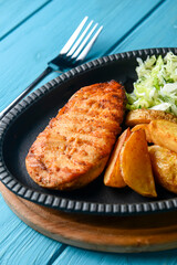 Grilled Chicken Steak with fried potatoes in rural style and coleslaw salad served in a tray over blue background.
