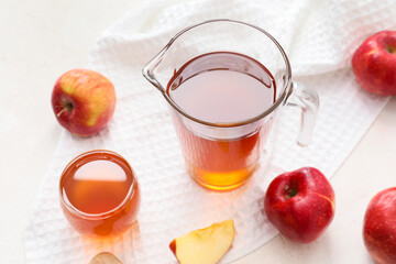 Glass and jug of apple juice with fresh fruits on light background