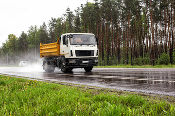A modern dump truck for transporting bulk cargo drives on the highway in rainy weather. Safe...