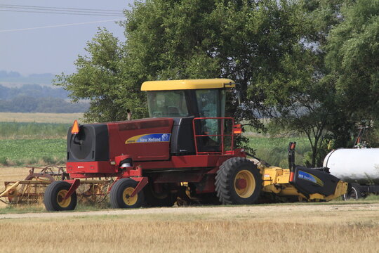New Holland Swather sitting in a farm field with blue sky and tree's on a summer day. South of Ellsworth Kansas USA.