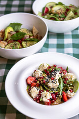 Green salad with cucumber, zucchini and strawberries in a white bowl over green plaid tablecloth.