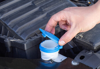 The man's hand opens the filler neck for filling the windshield washer fluid of a passenger car....