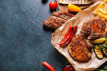 Tasty pork steaks and grilled vegetables on dark background