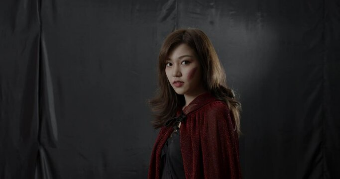 Mysterious Asian woman in red cape staring at camera with spooky eyes. Halloween costume party celebration around the world. Sexy and seductive girl in fantasy cosplay concept