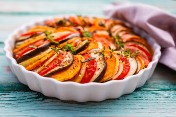 Delicious vegetable ratatouille in a white baking dish on a wooden background.