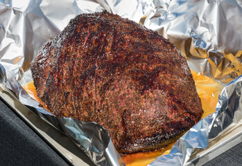 Portion of foil wrapped spicy seasoned beef brisket with juices