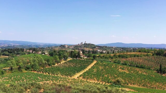 Tuscan countryside shot with drone at summer time of wine fields, small village in the background. Aerial view of amazing cultivated fields in hot weather, arid fields,green trees,olive trees 