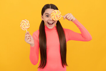 amazed teen girl with lollipop candy on stick on yellow background, sweet tooth
