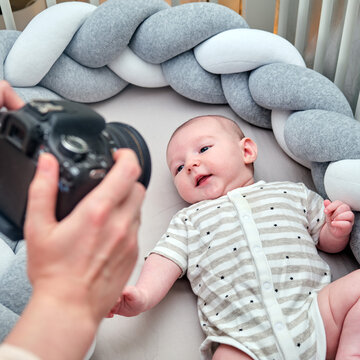 A photographer takes pictures of a newborn baby with a camera on the crib. Photo session of children in the home interior