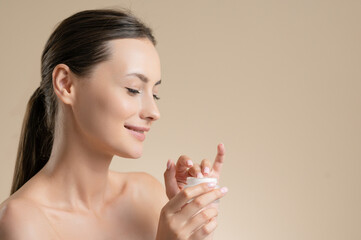Happy woman applying cream on face in studio