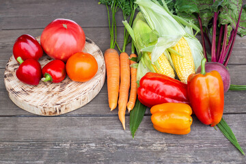 The autumn harvest grown in the garden bed lies on a wooden table. Tomatoes, carrots, bell peppers and corn with beets, natural vegetables