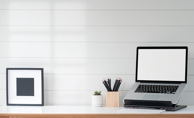 Fototapeta premium Mockup blank screen laptop on stand and wooden frame on wooden table with white wooden wall.