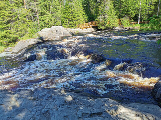 View of the bubbling waterfall with brown water on the Tokhmayoki River in Karelia from the ecological trail.