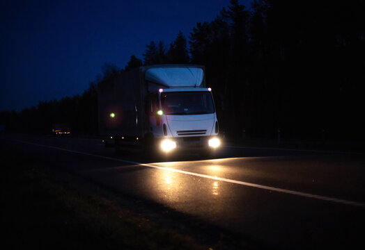 The van transports cargo with the headlights on at night, in the background. Freight industry, international