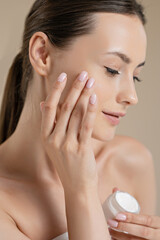 Young adorable woman using moisturising face cream