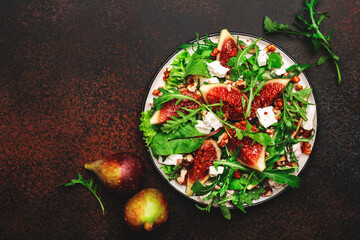 Salad with figs, goat cheese, walnuts, chard and arugula on brown background, top view, copy space