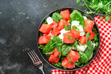 Watermelon salad bowl with soft goat cheese, spinach and pea sprouts on gray background, top view, copy space
