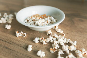 a plate of popcorn grains and ready-made white popcorn sprinkled on a wooden table