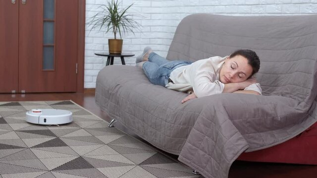 Relax with your home robot. The female sleeps on the couch while the robot cleans the carpet.