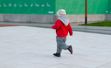 A little boy in a red jacket runs in the park with his back to the camera, loves to run since childhood