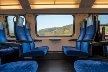 Blue empty opposing seats in a moving train. Large window with blurred landscape, daytime, summer, no people.