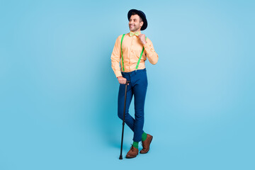 Full size photo of brunet man with cane look empty space wear cap shirt trousers socks shoes isolated on blue color background