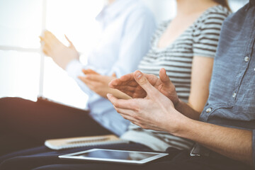 Business people clapping at meeting or conference, close-up of hands. Group of unknown businessmen and women in sunny office