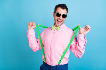 Photo of fancy brunet hairstyle man touch suspenders wear eyewear pink shirt isolated on blue color...