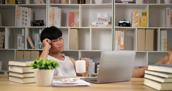 Bored freelancer man in singlet works on laptop and drinks coffee