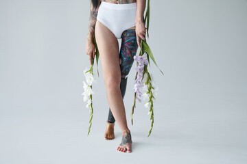 Disabled tattooed woman with prothesis leg standing with flowers at the studio
