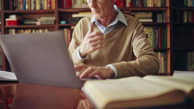 Man in his 50s working on project on laptop, using books and wi-fi at library