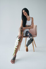 Woman with artificial leg sitting at the chair while posing at the studio with flowers