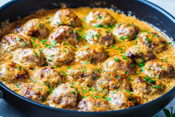Swedish meatballs in creamy sauce in black frying pan, gray background. Scandinavian food concept.